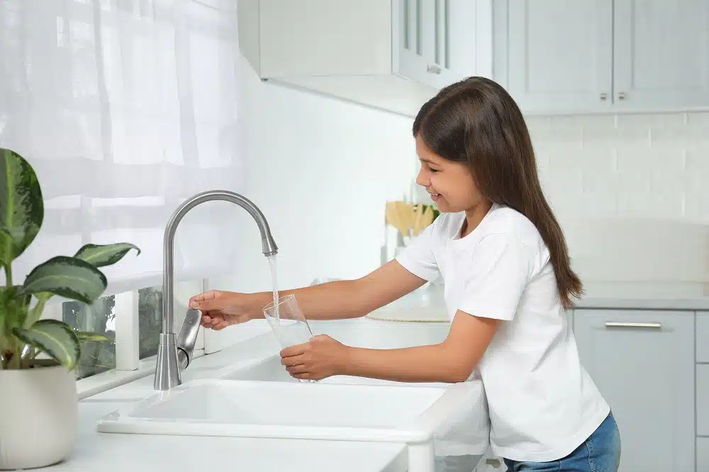 girl filling glass with water from tap in kitchen