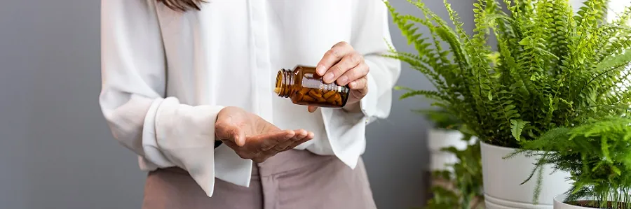 cropped shot of a young woman taking medication at home. woman holding pills or vitamins in open hand while taking morning medication