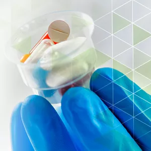 scientist gloved hand holding clear plastic cup of medicines