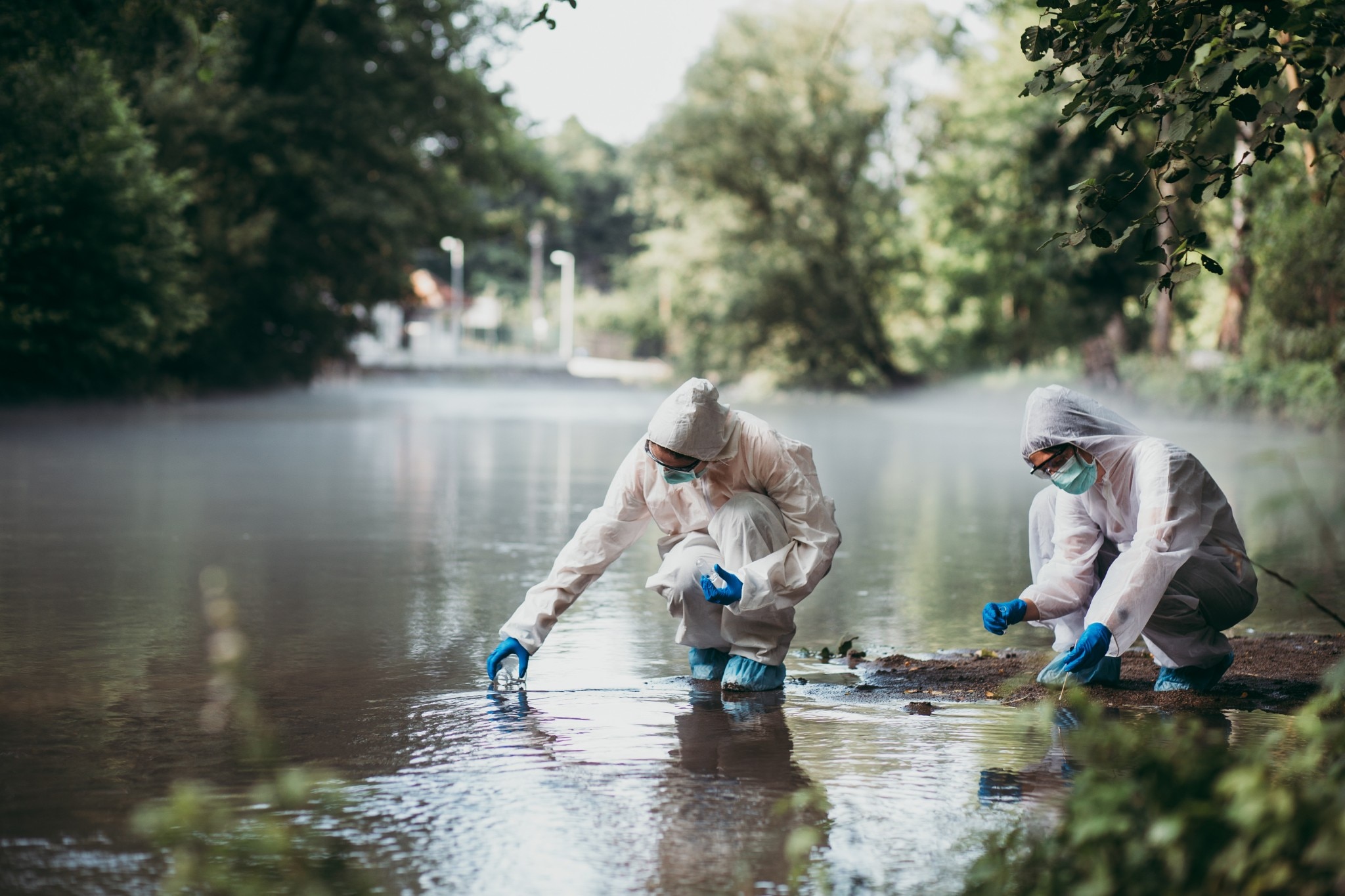 Zwei Wissenschaftler in Schutzkleidung nehmen Wasserproben aus dem Fluss